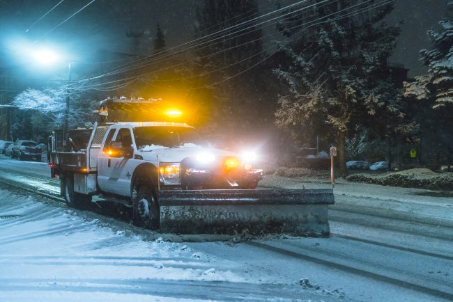 A snowplow on a snowy street at night.